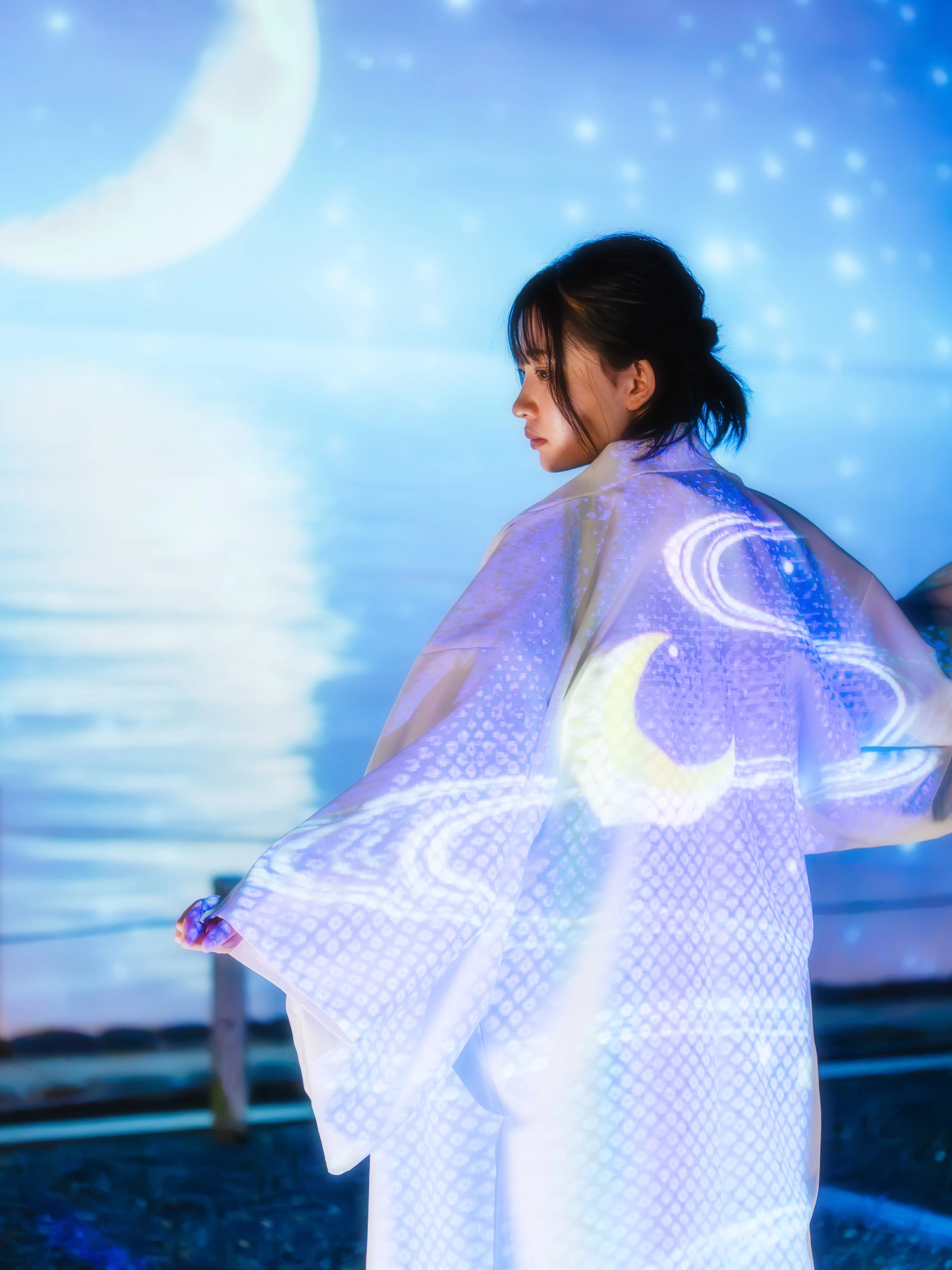 三日月と星の映像を身にまとった、白い着物姿の女性の後ろ姿