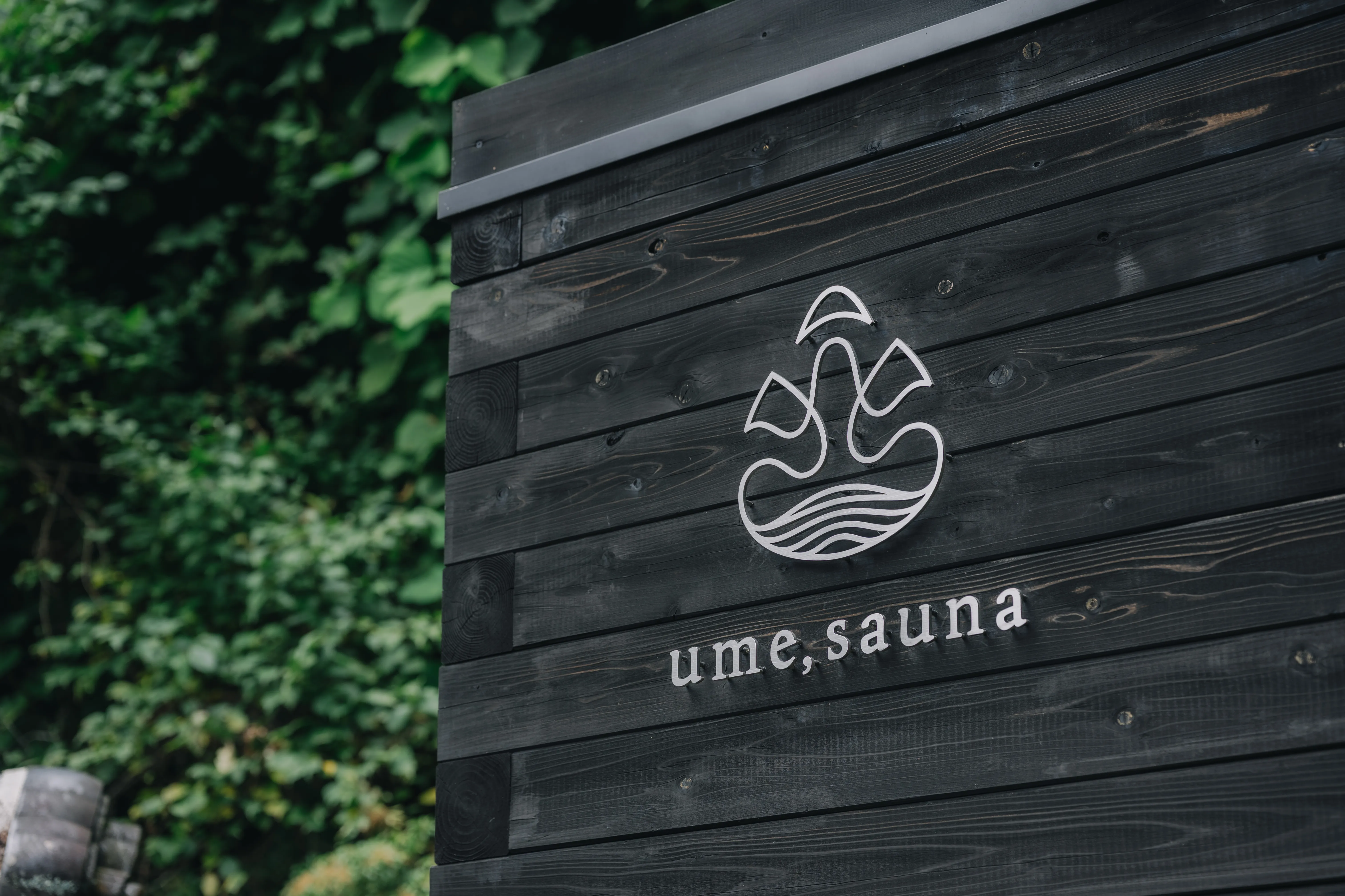 黒い板壁に掲げた ume,sauna のサイン